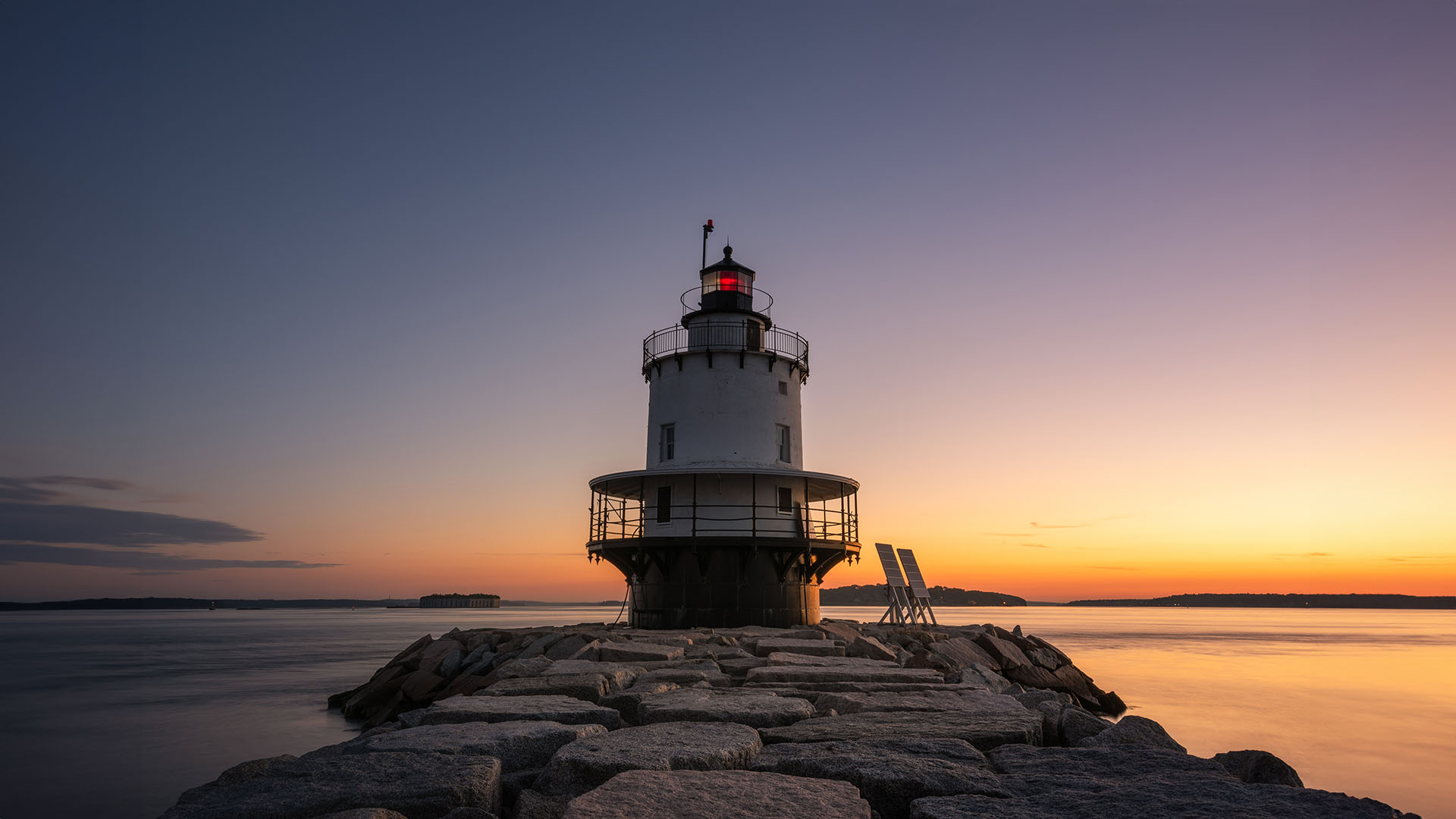 The image shows a lighthouse at sunset with the sky transitioning from warm hues to cooler tones, and the lighthouse is illuminated against the backdrop of the setting sun.