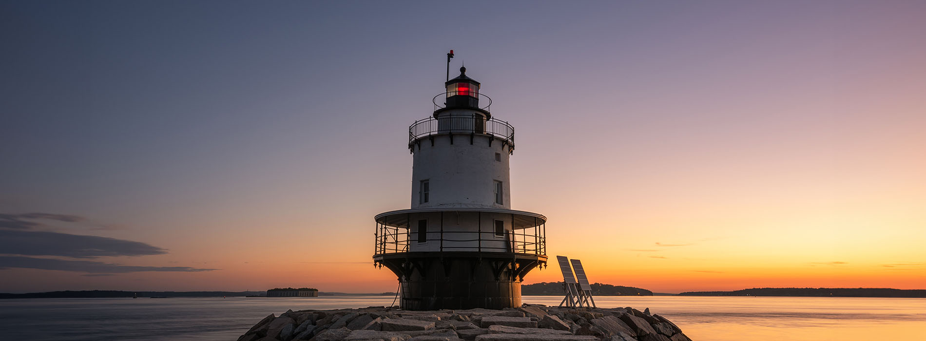 Lighthouse at sunset with a clear sky, calm water, and a tranquil atmosphere.