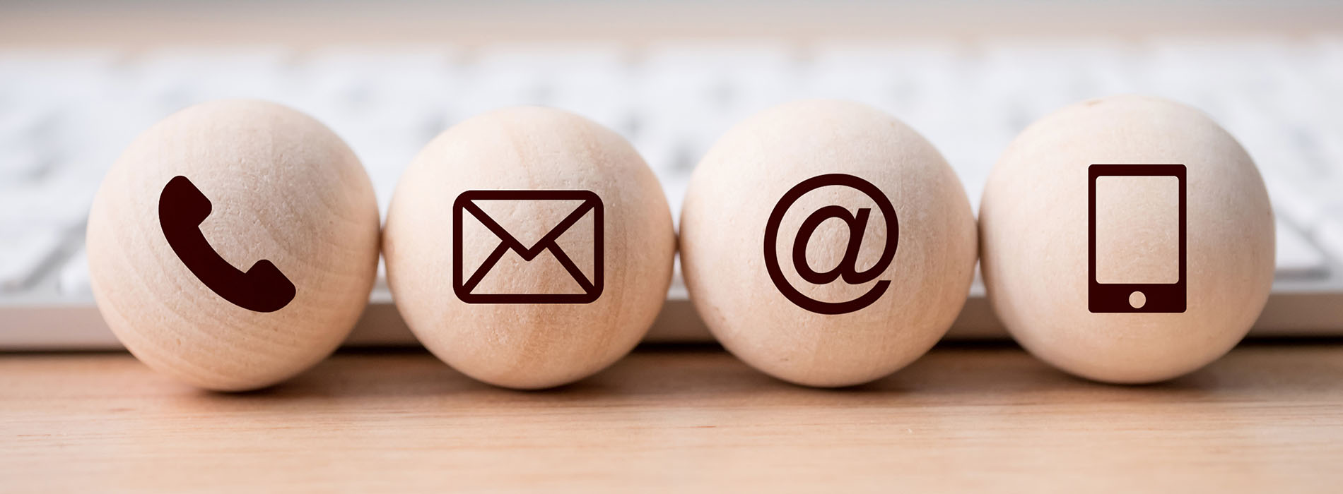 The image shows a collection of wooden balls with various icons and text on them, arranged in a row, representing different communication methods such as email, phone call, and social media, placed against the backdrop of a keyboard.