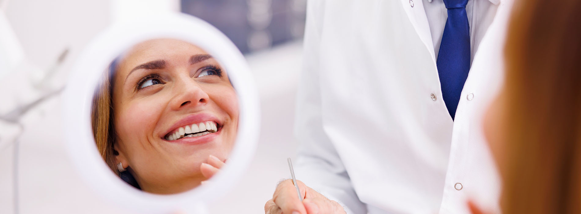 A woman receiving a dental check-up, with a smiling dentist holding up a mirror to show her teeth.