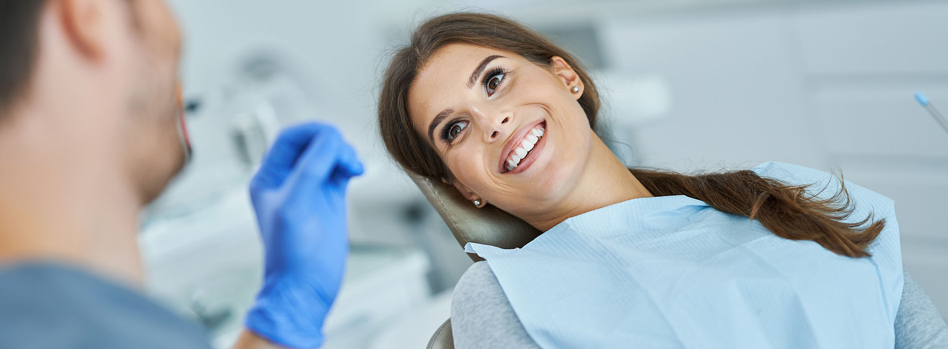 A dental professional is smiling as they assist a patient in a dental office.