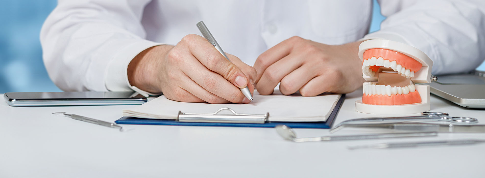 The image depicts a person sitting at a desk with various dental tools and equipment, focusing on papers and models related to dentistry.