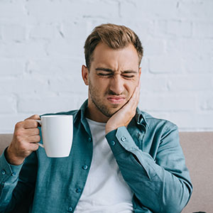A man in a casual setting, holding a coffee cup and looking away with a slight frown.