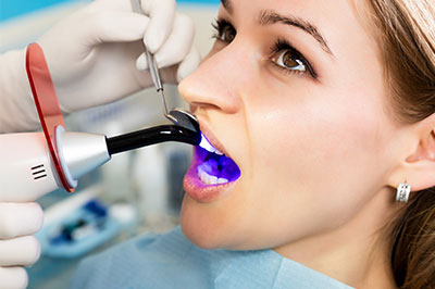 A woman in a dental chair receiving teeth cleaning, with a dentist using an ultrasonic scaler and a purple mouthwash.