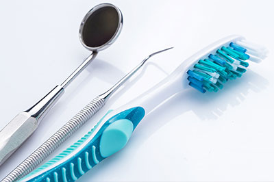 The image displays a collection of dental tools, including a toothbrush with blue bristles and a pair of scissors, set against a white background.