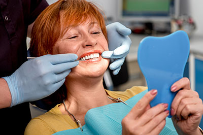 The image shows a woman sitting in a dental chair, receiving dental care, with a smile on her face.