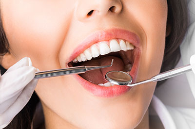 A woman with a toothy smile is wearing a white lab coat and holding a dental tool, likely in the context of dental care or promotion.