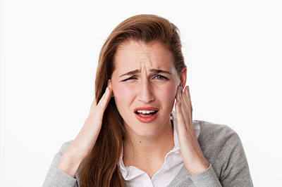 The image is a photograph of a woman with her hand on her head, appearing to be in pain or discomfort.