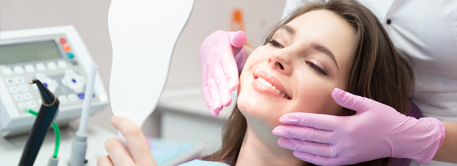 The image shows a woman sitting in a dental chair, receiving dental care from a professional who appears to be cleaning or examining her teeth.