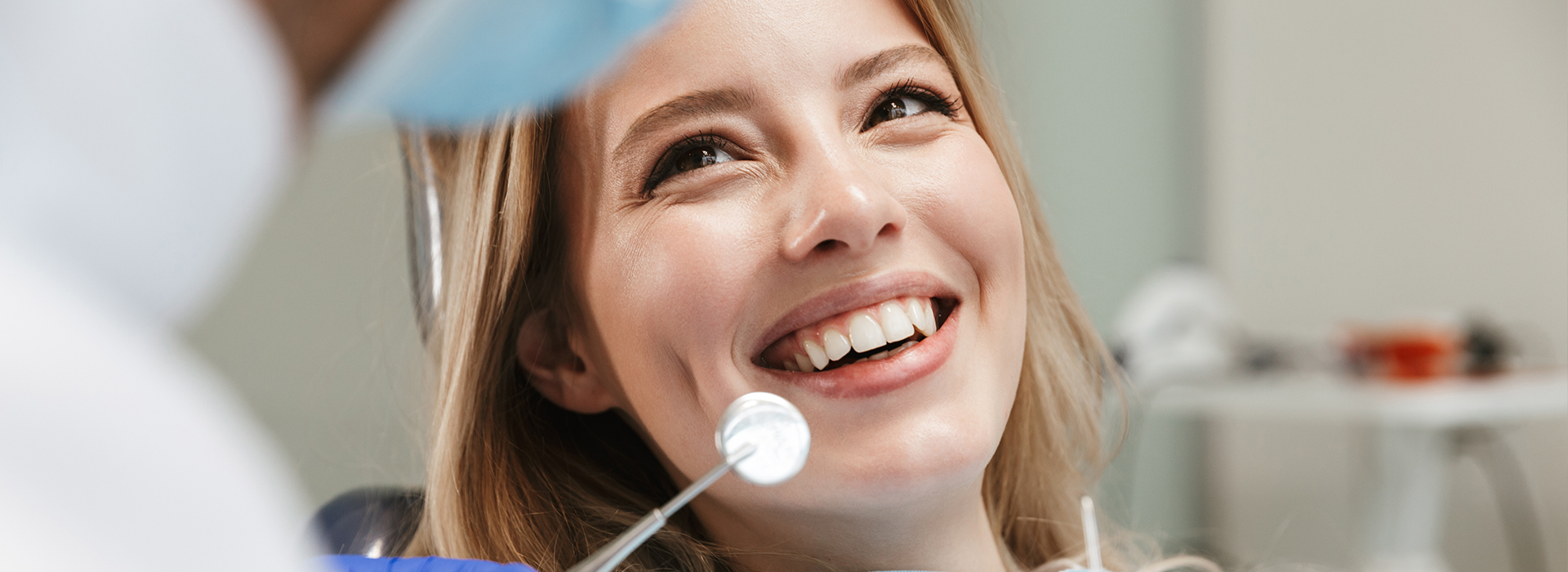 A woman is smiling in a dental office setting, with a dentist working on her teeth.