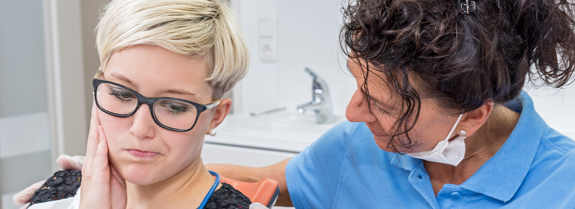 The image shows a woman in an orange shirt attending to a patient wearing glasses, with another person observing the process.