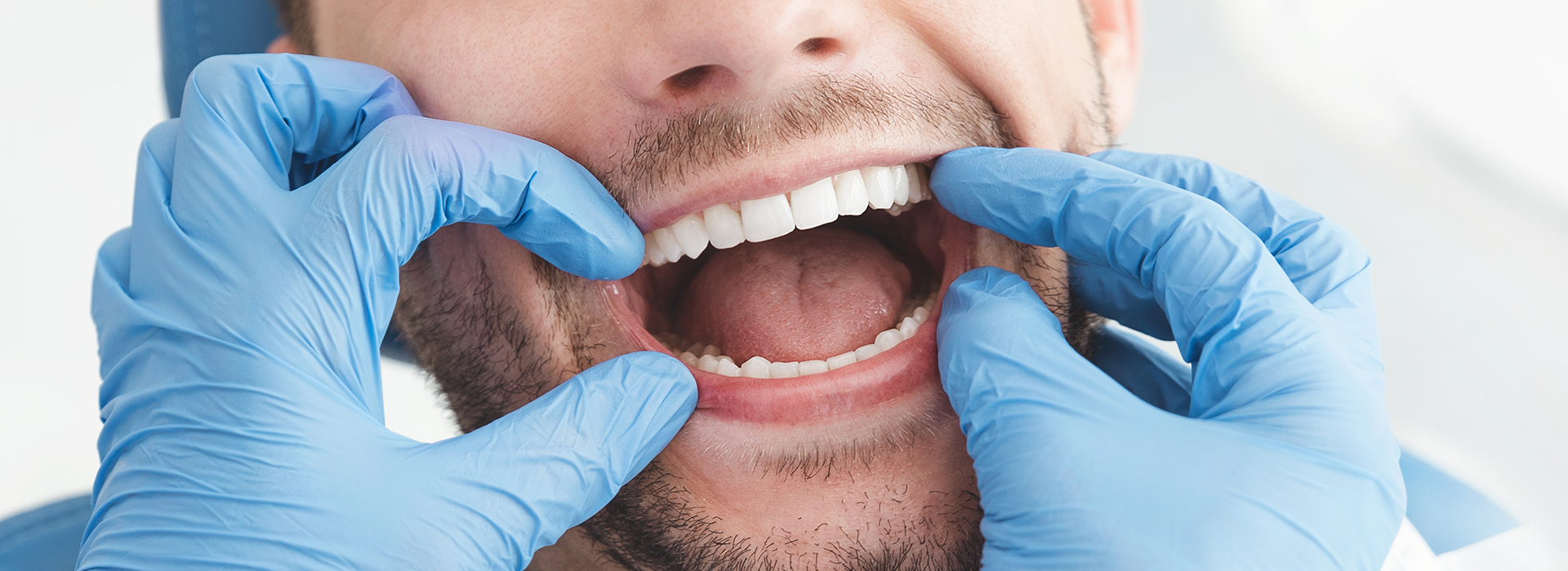 Dental professional in blue gloves holding a model mouth open, smiling.