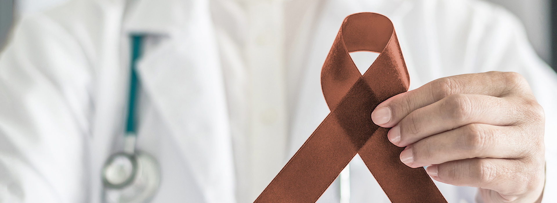 The image shows a person wearing a white lab coat holding up a red ribbon with a symbol on it, which is commonly associated with awareness for a specific health condition.