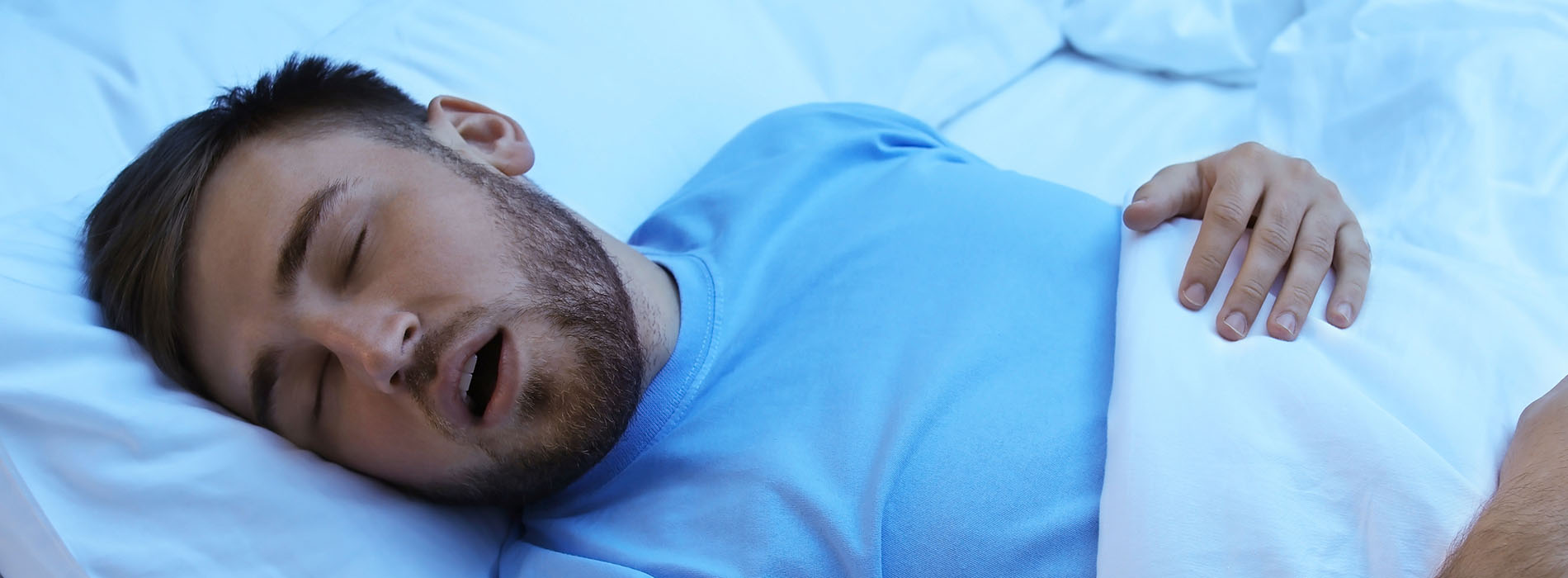 The image shows a man lying in bed with his mouth open, appearing to be asleep or unconscious.