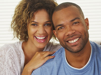 A man and a woman smiling at the camera, with the man wearing a blue shirt and the woman in white.