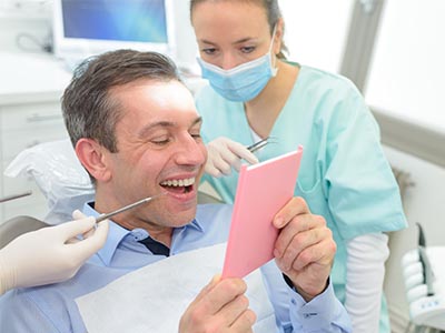 A man holding a smartphone while sitting in a dental chair, with a woman in scrubs looking on.