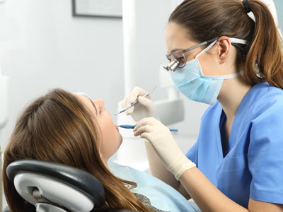 The image shows a dental professional assisting a patient during a dental appointment, with the patient seated in a chair and the professional standing behind.