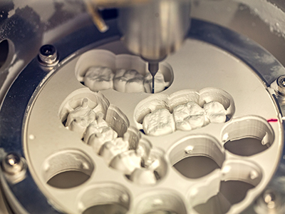 The image shows a close-up of a dental implant being manufactured or processed, with various components and machinery visible in the background.