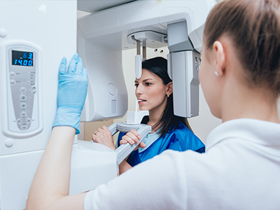 Woman in blue uniform standing next to a large, modern MRI machine with a technician.