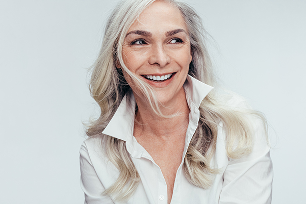 The image depicts a woman with short hair, wearing a white blouse and smiling at the camera.