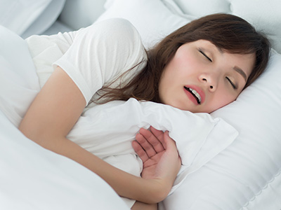 A woman asleep in bed with a pillow over her mouth.