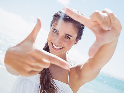 A woman is taking a selfie with her hand in front of her face, smiling at the camera.